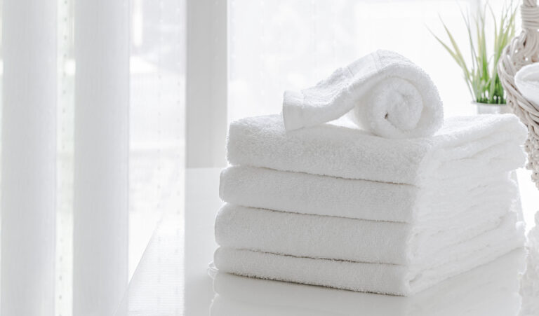 Clean white towels on white table in white room, copy space.